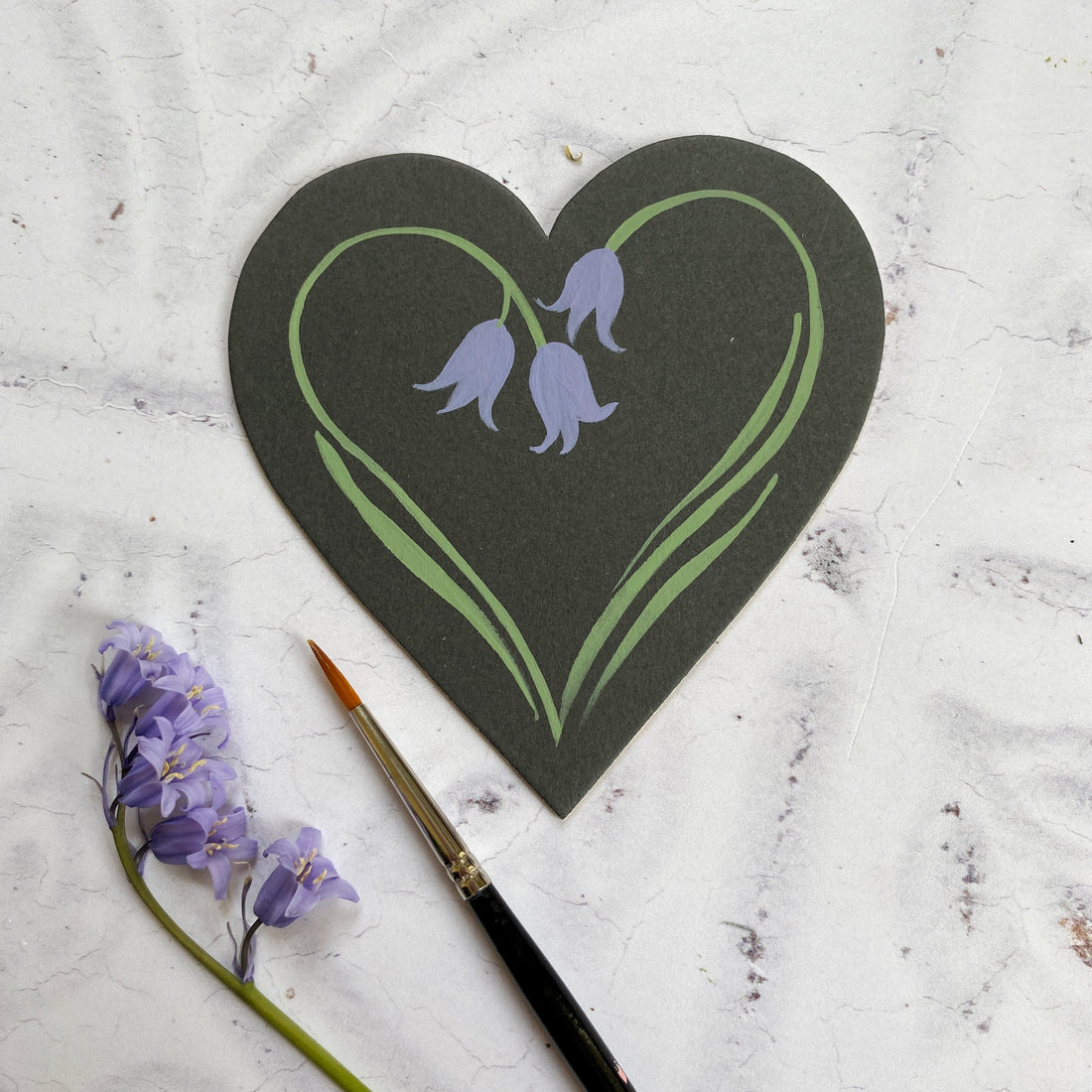 Painted bluebell heart from You Can Folk It next to a paintbrush and bluebells